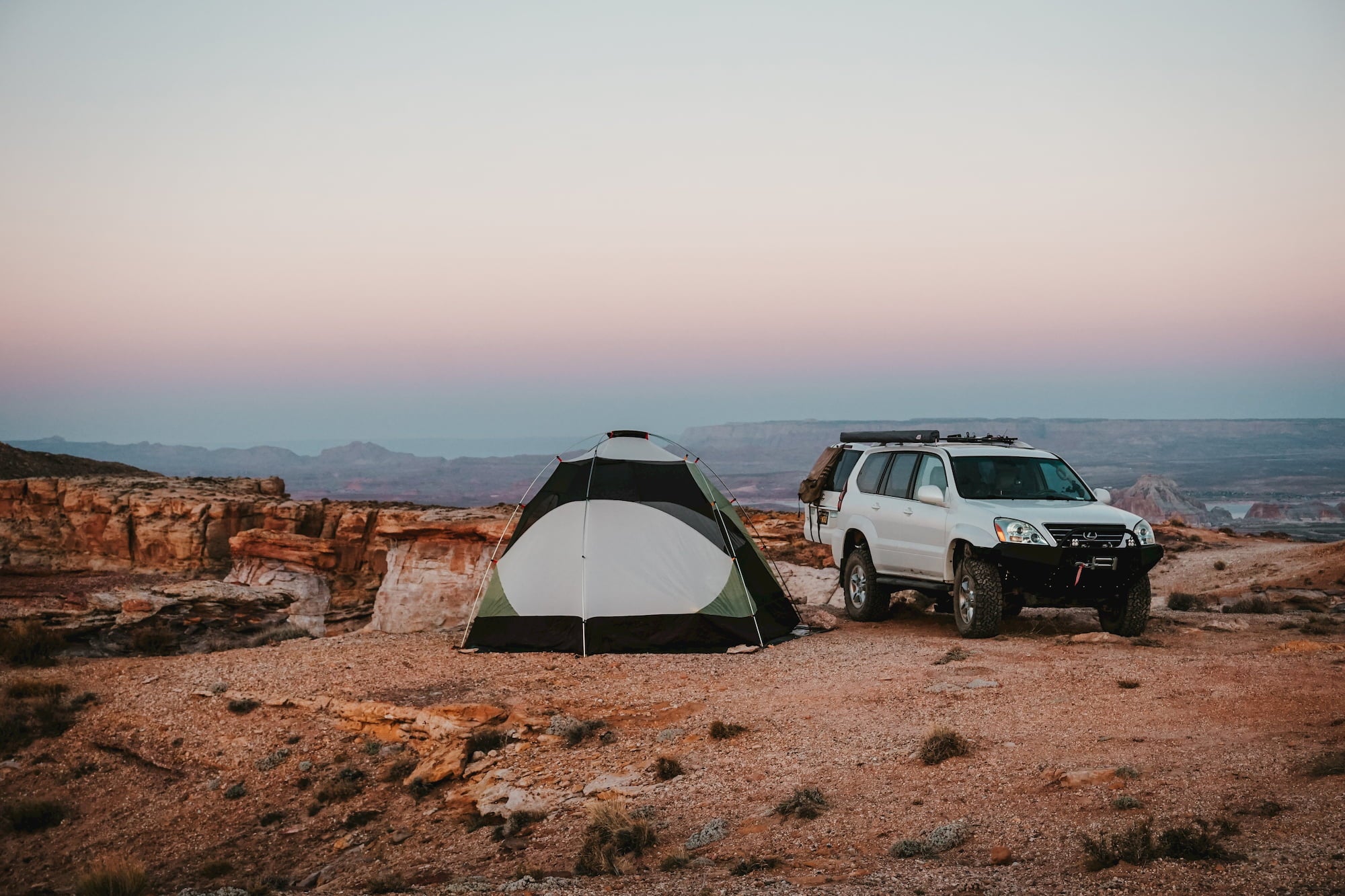 Car parked beside tent on open desert land.